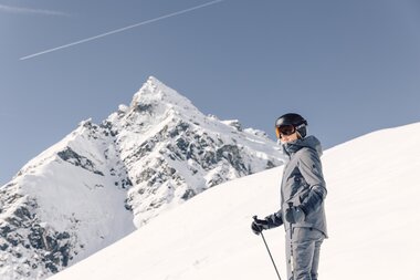 Skifahrerin in grauer Jacke und Helm blickt vor einem spitzen, schneebedeckten Berggipfel "die Madrisa" in die Ferne. | © Gargellner Bergbahnen, Daniel Zangerl