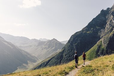 Wanderung auf den Gargellner Schafberg Wegen | © Gargellner Bergbahnen GmbH & Co KG, Daniel Zangerl Zwei Erwachsene wandern auf einem schmalen Bergweg am Gargellner Schafberg. Im Tal und an den Hängen leuchten grüne Wiesen, umrahmt von imposanten Berggipfeln. | © Gargellner Bergbahnen GmbH & Co KG, Daniel Zangerl