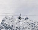 Zwei Gondeln der Schafbergbahn in Gargellen schweben vor einer beeindruckenden, schneebedeckten Bergkulisse. Die modernen Kabinen der Gargellner Bergbahnen heben sich klar vom hellen Winterhimmel ab, während im Hintergrund die majestätischen Gipfel der Montafoner Alpen aufragen. | © Gargellner Bergbahnen GmbH & Co KG, Daniel Zangerl
