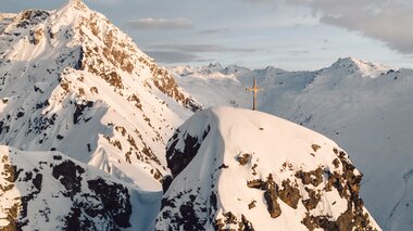 Gipfelkreuz im Winterlicht – Stille über Gargellen | © Gargellner Bergbahnen GmbH & Co KG, Daniel Zangerl Gipfelkreuz auf einem verschneiten Berggipfel bei Gargellen im warmen Licht der Abendsonne. | © Gargellner Bergbahnen GmbH & Co KG, Daniel Zangerl