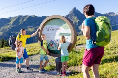 Golmis Forschungspfad am Erlebnisberg Golm | © Golm Silvretta Lünersee Tourismus GmbH Bregenz, Stefan Kothner Eine funfköpfige Familie die am Erlebnisberg Golm auf Golmis Forschungspfad wandert und auf eine runde Tafel blickt auf der steht, wie man Golm Forscher wird | © Golm Silvretta Lünersee Tourismus GmbH Bregenz, Stefan Kothner