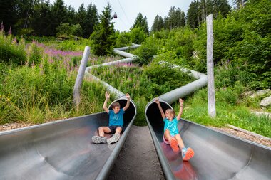 Waldrutschenpark-Golm im Montafon | © Golm Silvretta Lünersee Tourismus GmbH Bregenz, Mathäus Gartner Zwei Kinder die gerade aus zwei einzelnen Rutschen am Waldrutschenpark-Golm rutschen | © Golm Silvretta Lünersee Tourismus GmbH Bregenz, Mathäus Gartner